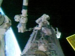 Atlantis Astronauts work on the Space Station's S1 Truss during the first of three STS-112 spacewalks. A corner of one of the Station's solar arrays is visible at right. NASA TV capture.