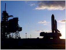 As the sun rises from below the horizon on the right, Space Shuttle Discovery crawls up to Launch Pad 39A and its resting spot next to the Fixed Service Structure, which is seen on the left. Photo coutesy of NASA.